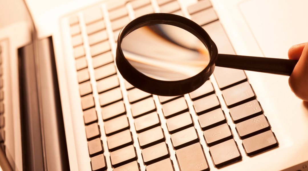 Magnifying glass being held over a laptop keyboard.